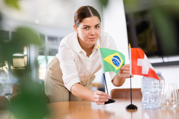 Jovem Assistente Montando Bandeiras Suíça Brasil Mesa Para Negociações Internacionais — Fotografia de Stock