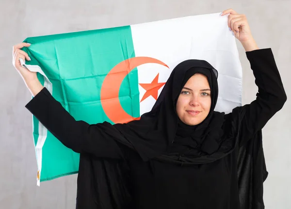 アルジェリアの旗を保持する黒の伝統的なヒジャブを着用して陽気な若いイスラム教徒の女性 — ストック写真