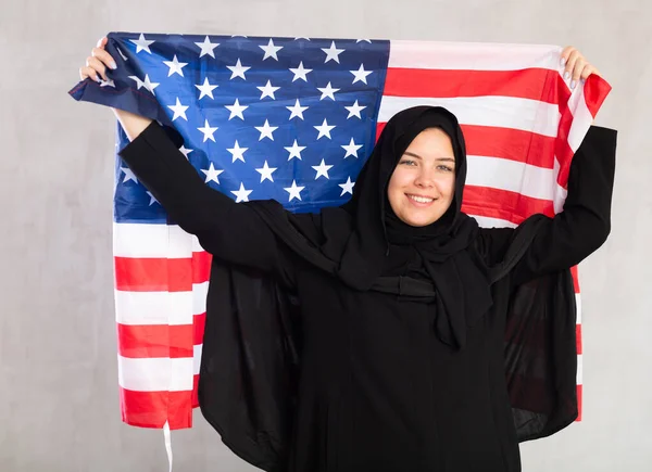 アメリカの国旗を掲げる黒い伝統的なヒジャブを身に着けている陽気な若いイスラム教徒の女性 — ストック写真