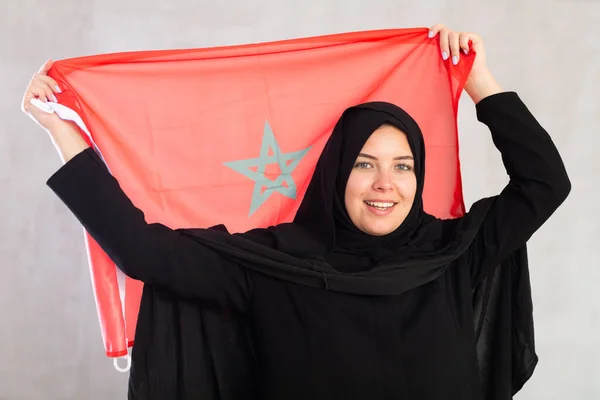 モロッコの旗を掲げる黒い伝統的なヒジャブを身に着けている陽気な若いイスラム教徒の女性 — ストック写真