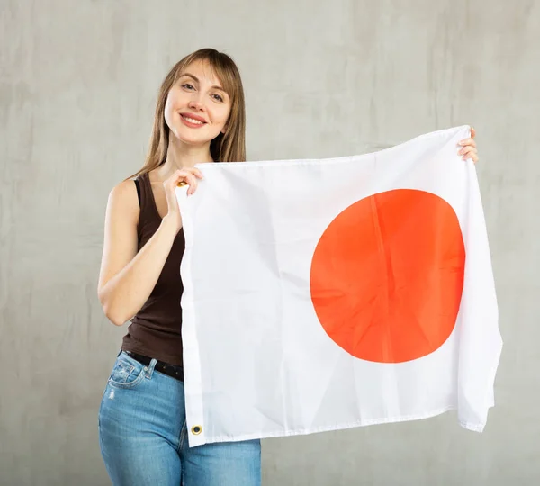 Uśmiechnięta Młoda Kobieta Machająca Narodową Japońską Flagą Podczas Pozowania Szarym — Zdjęcie stockowe