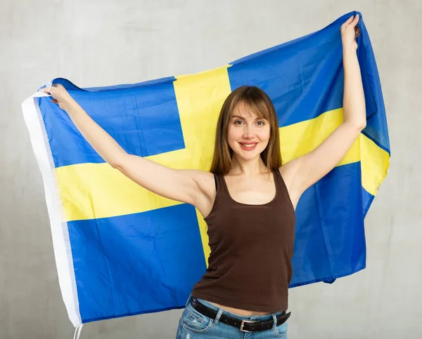 スウェーデンの大きな旗を持つ幸せな若い女性は 光の無色の背景に喜んでポーズ — ストック写真