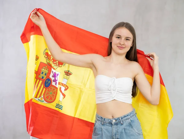 大きなスペイン国旗を手に持っている少女 若い十代の少女は肩を引っ張り スペイン国旗の布に身を包んだ スタジオショット グレーバック — ストック写真