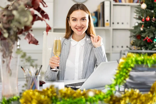 シャンパンのガラスを持つ女性マネージャーはオフィスでインターネット上でメリークリスマスを祝います — ストック写真
