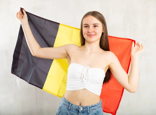 信实而积极的年轻女子举着比利时的大旗 带着自信的微笑露出牙齿 劳动力外流 出国留学 没有边界的世界 灰色背景拍摄 — 图库照片
