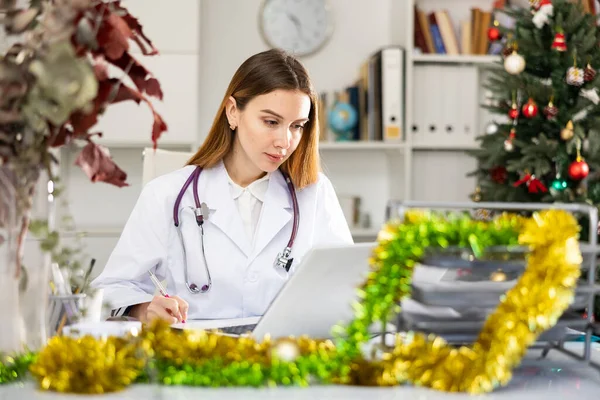 クリスマスの間にラップトップコンピュータを使用して医務室で働く正の女性医師 — ストック写真