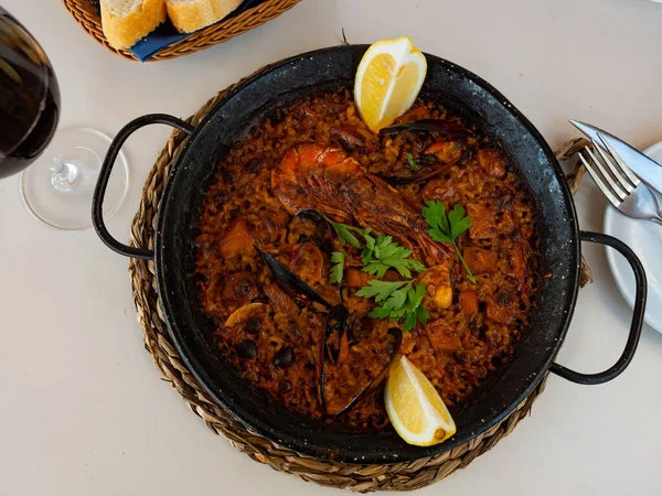 Fresh hot paella with seafood in cast-iron pan. There is cast-iron baking dish with hot lunch on stand for hot. Gastro tourism, acquaintance with culinary traditions of countries, gourmet restaurant