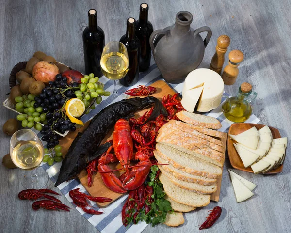 Appetizing smoked sturgeon with lobster, crayfishes, bread, cheese, fruits and wine on wooden surface