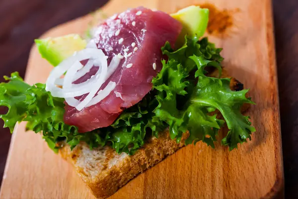 Toasted bread with raw tuna steak, salad, avocado and onion rings