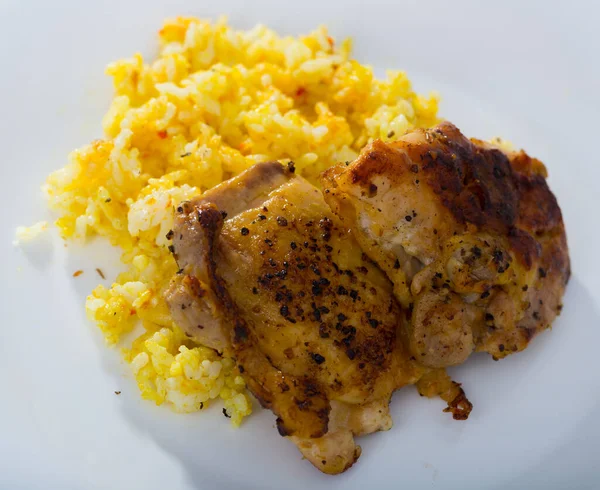 Baked chicken thighs with spicy rice served on white plate..
