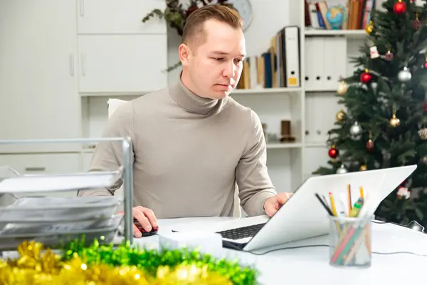 Executive man working in office during Christmastime. Man using laptop in decorated workplace.