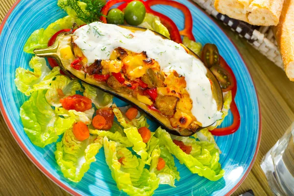 Eggplant stuffed with vegetables and baked with cheese, served with lettuce at plate
