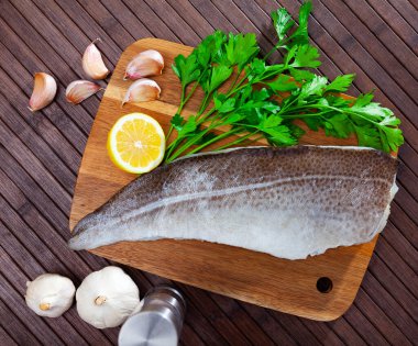 Fresh cod fillet on wooden surface with seasonings ready for cooking.. clipart