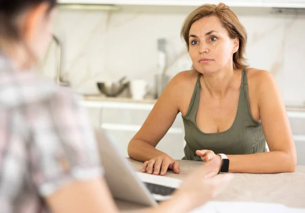 Middle-aged woman agent communicating kindly with female business-partner sitting at the kitchen-table