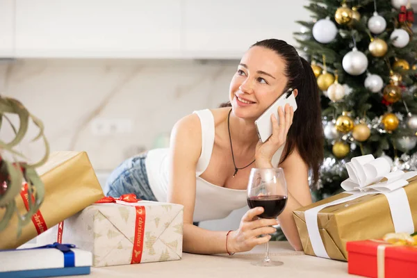 young woman is relaxing at home with glass of wine during New Year holidays. She talks on phone
