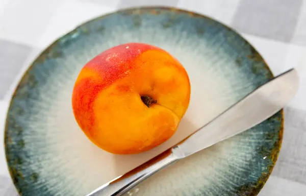 Fresh yellow peach for dessert served on plate with knife.