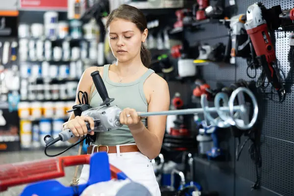 Young female buyer chooses mixer for building mixtures in local hardware store