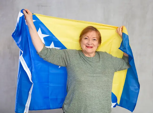 快乐成熟的女士自豪地站在那里高举波士尼亚国旗 — 图库照片