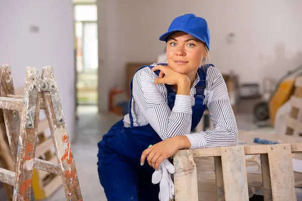 修屋过程中穿着蓝色工作服的心满意足的年轻女建筑工人的画像 — 图库照片