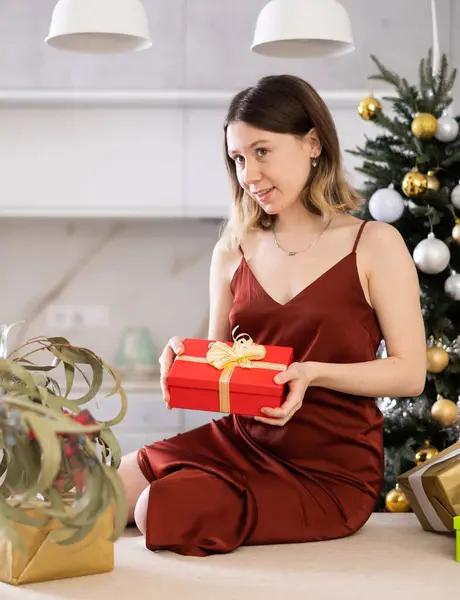Pozitivní Mladá Žena Dárečkem Rukou Pózuje Doma Pozadí Vánočního Stromečku — Stock fotografie