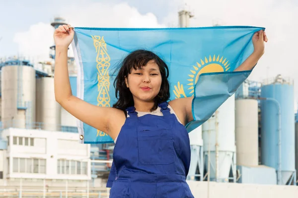 在现代化冶金厂的背景下 穿着工作服的女孩手中拿着哈萨克斯坦国旗 — 图库照片