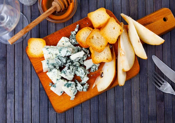 Blue cheese served on wooden board with honey, slices of pear and bread.