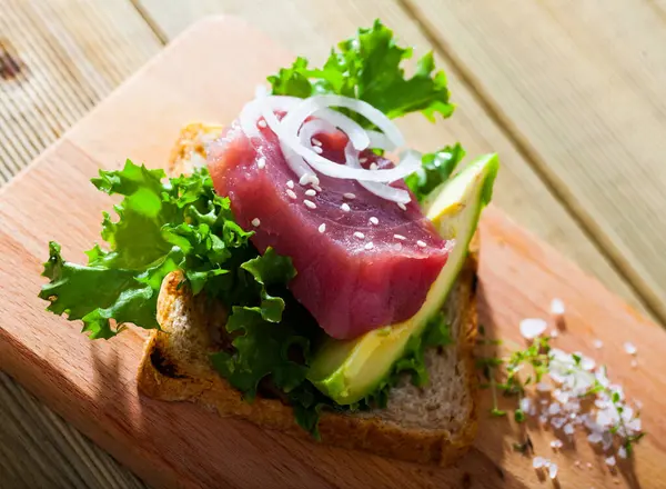 Toasted bread with raw tuna steak, salad, avocado and onion rings