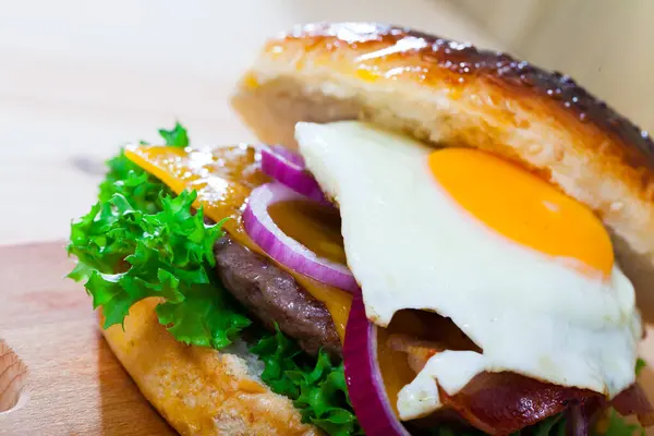 Appetizing cheeseburger with grilled beef patty, fried egg, bacon slice and fresh vegetables..