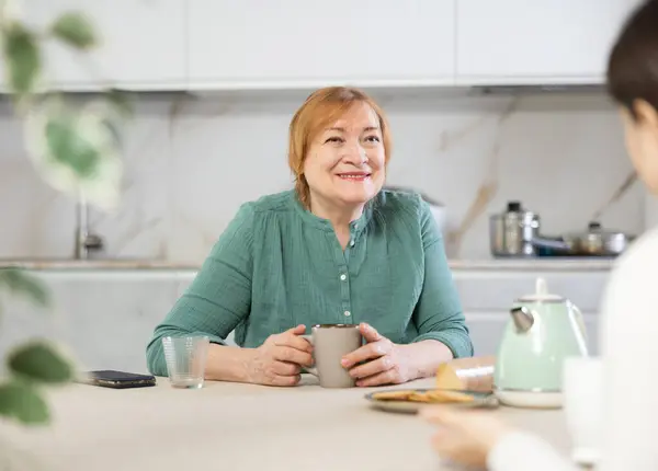 Happy older lady chatting in kitchen with warm smile