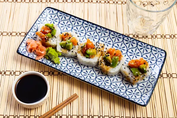 Sushi set - saketaki roll is served in white plate with blue pattern, topped with pickled ginger petals and pinch of spicy wasabi pieces. Traditional Japanese Asian cuisine, gastronomy