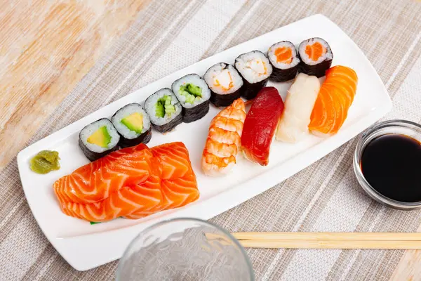 Sushi set maki rolls with salmon sashimi and nigiri is served in white narrow rectangular plate. Traditional Japanese Asian cuisine, gastronomy tourism