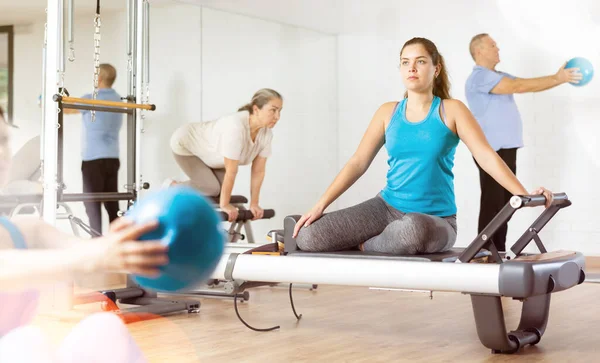 Concentrated young female in active wear training and using Pilates performer bed in gym