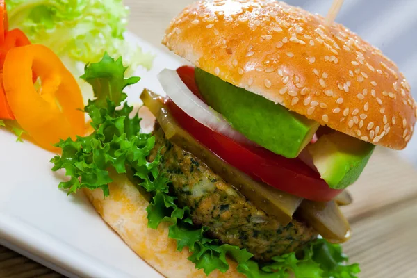 Tasty burger with vegan cutlet, lettuce, avocado, onion, tomato, pickled cucumbers