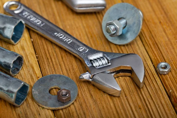 Adjustable wrench with bolts and melallic tools on wooden surface