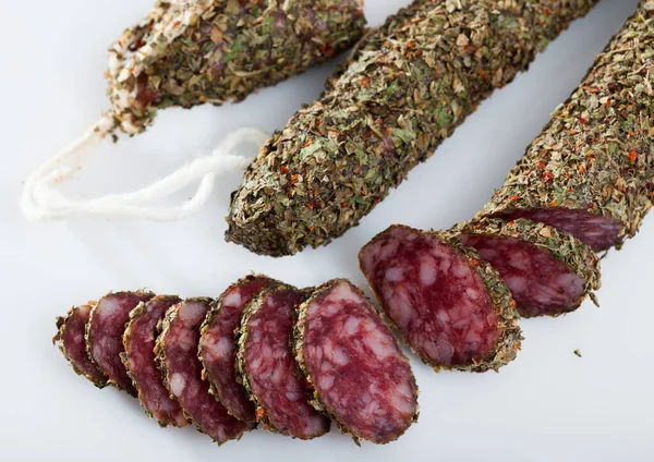 Image of spanish fuet with herbs sausages cut in slices on a white surface, close-up