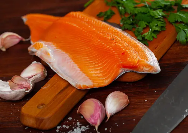 Raw fresh red trout fillet with garlic and greens on wooden table