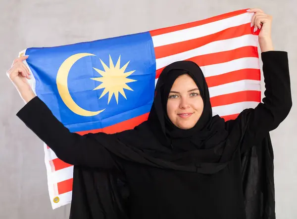 マレーシアの旗を掲げる黒い伝統的なヒジャブを身に着けている陽気な若いイスラム教徒の女性 — ストック写真
