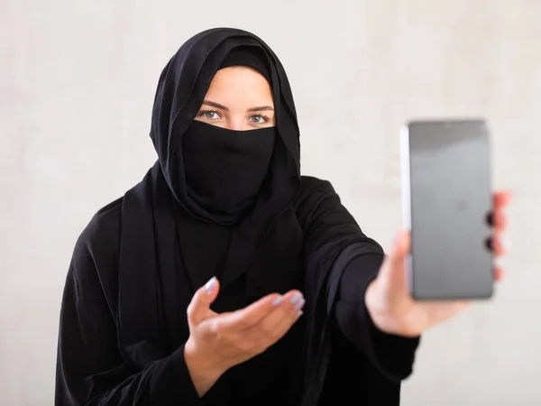 新しい携帯電話を披露する黒の伝統的なニカブを着用している若いイスラム教徒の女性 — ストック写真