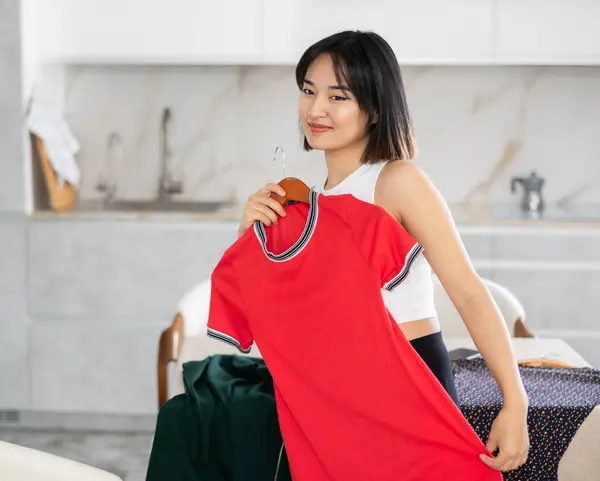 Mutlu Genç Asyalı Kız Mutfaktaki Masada Duran Elbiseyi Seçmeye Çalışıyor — Stok fotoğraf