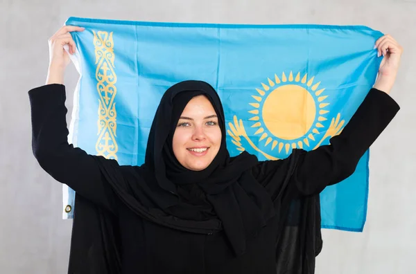 カザフスタンの国旗を持つ黒い伝統的なヒジャブを身に着けている陽気な若いイスラム教徒の女性 — ストック写真