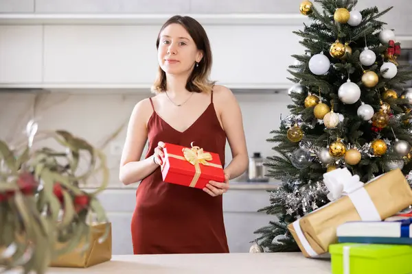 Positive young woman with a present in her hands poses at home against the background of a Christmas tree
