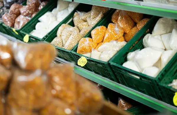 Various bulk food products, dried corn kernels and nuts, packed in poly bags, arranged in plastic crates on shelves in grocery store
