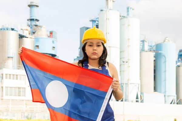 穿着硬礼帽站在工厂前打着老挝国旗的亚洲姑娘 — 图库照片