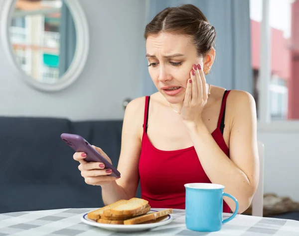 Dissatisfied woman with toothache sitting at dinner table at home