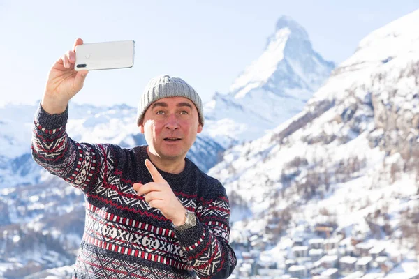 Positive travel blogger using smartphone to record vlog while hiking in snow covered Swiss Alps in wintertime on sunny day..