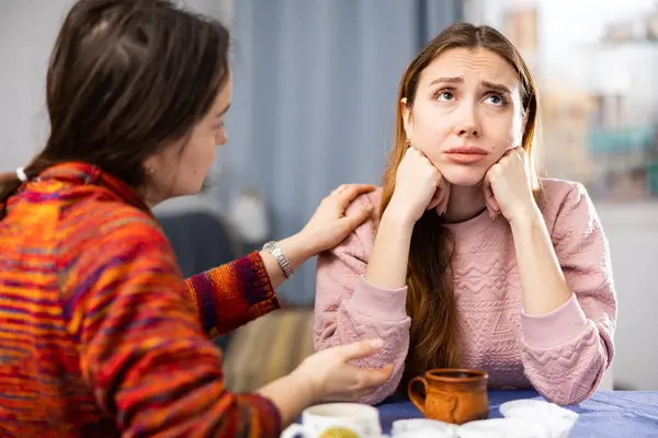 Woman comforting her female friend who sitting at table and feeling depressed.