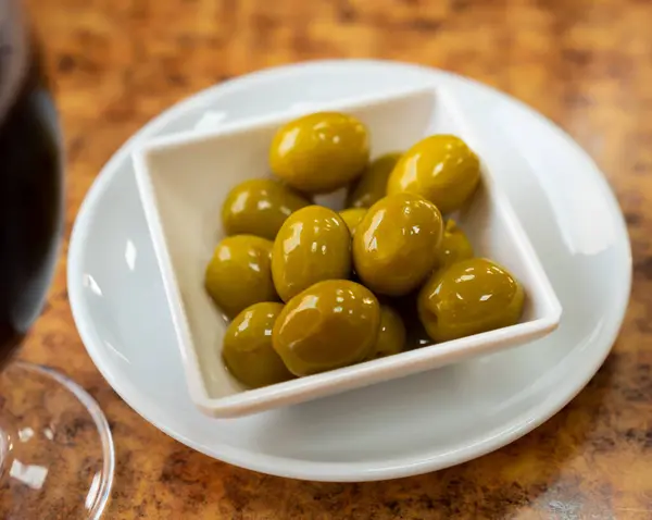 Appetites are waiting on table, light snack - bowl with pickled green olives. Traditional vegetable addition to main dishes, snacks and alcoholic beverages