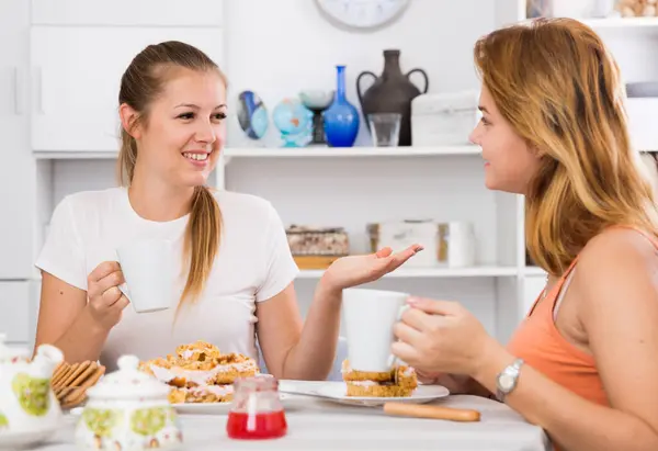 Young women are meeting for gossips on the kitchen at home.