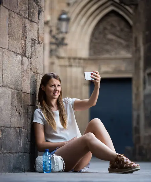 Szczęśliwa Młoda Kobieta Robi Selfie Siedząc Pobliżu Starego Kamiennego Muru — Zdjęcie stockowe