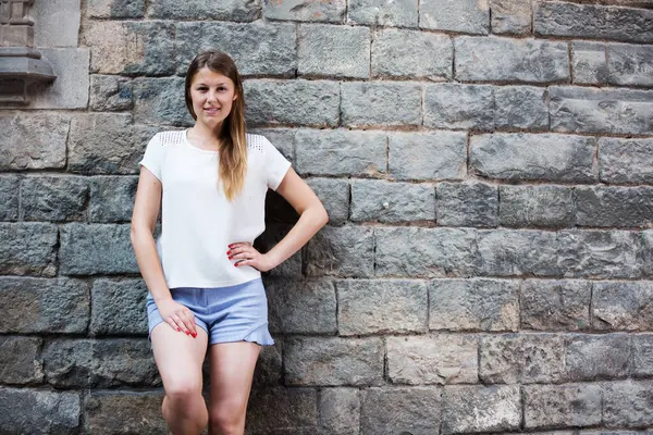 快乐的年轻女子站在石墙的背景上在城市里漫步 — 图库照片